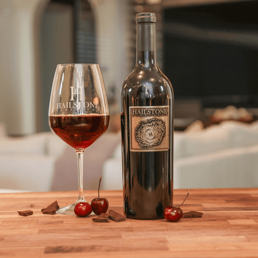 A glass full of 2020 Proprietor's Reserve Cabernet Sauvignon on a Wood Table with the Bottle to the Right of it