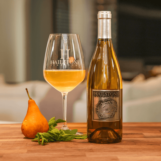 A glass full of 2021 Restoration Chardonnay on a Wood Table with the Bottle to the Right of it