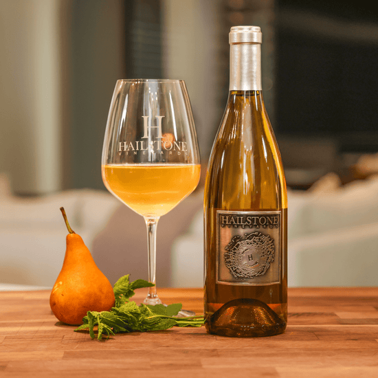 A glass full of 2021 Restoration Chardonnay on a Wood Table with the Bottle to the Right of it