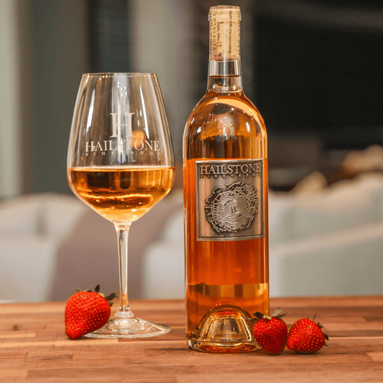 A glass full of Weather Dancer Dry California Rosé on a Wood Table with the Bottle to the Right of it